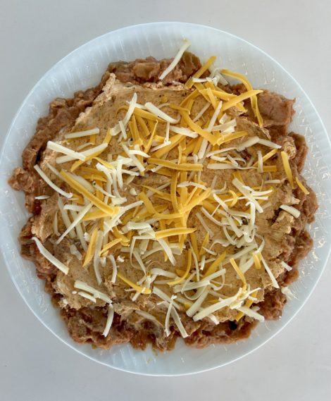 Layer the seasoned cream cheese and shredded cheese on top of the refried beans